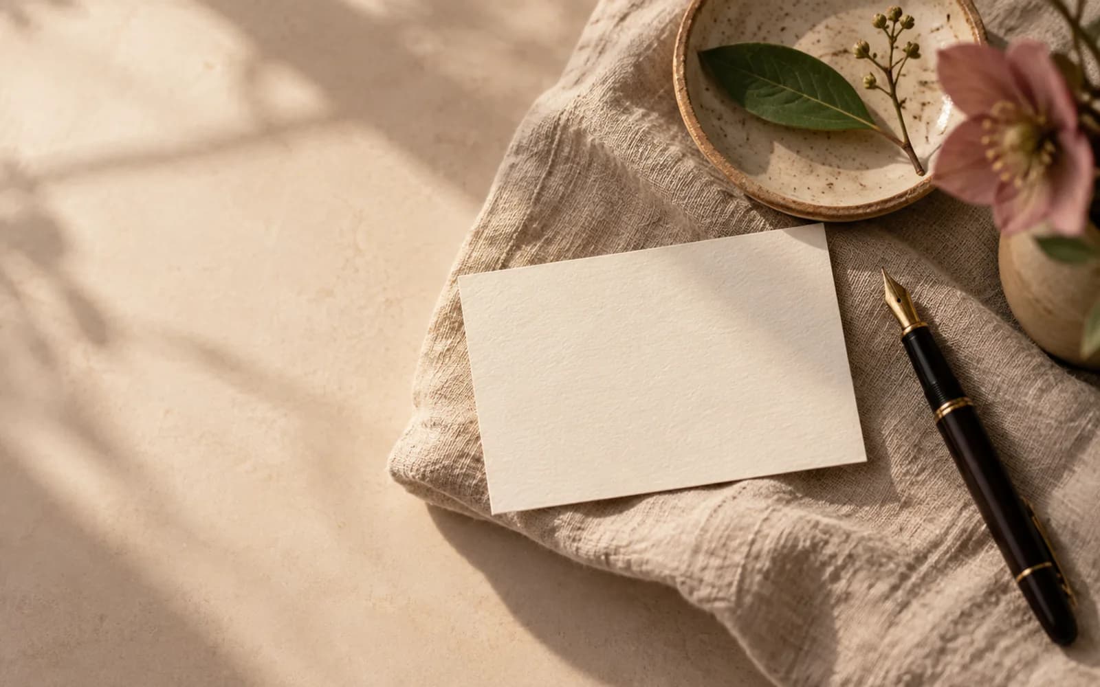 A blank cream card, pen and green sprig in warm light.
