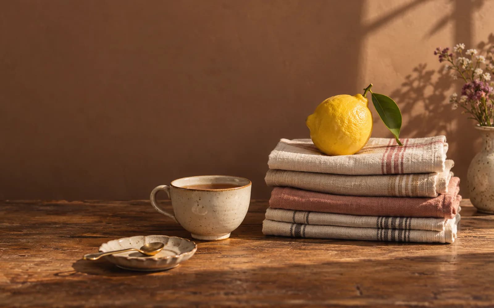 A lemon perched on folded tea towels beside a cup of tea.